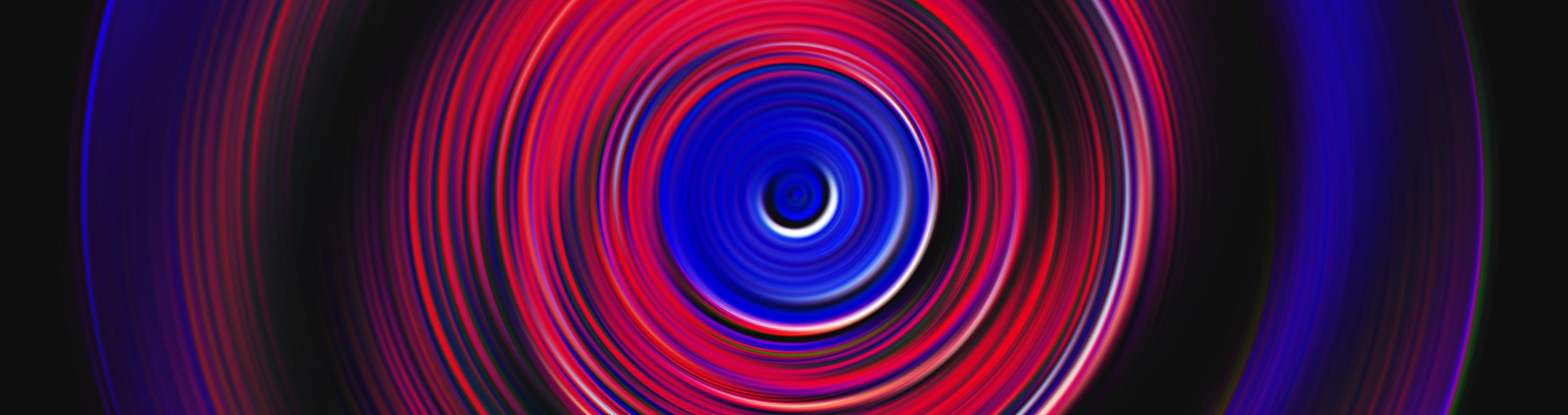 A swirling abstract pattern with concentric circles in shades of red and blue on a black background.