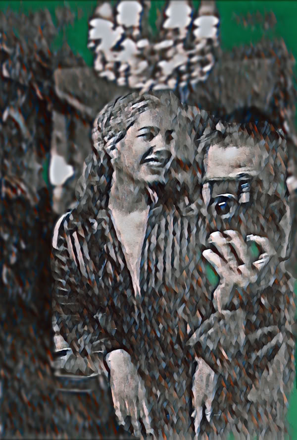 A black and white image of a woman smiling and a person taking a photo with a camera, with a chandelier visible in the background.